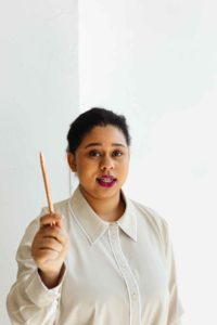 Woman with dark hair holding a pencil upright in front of her.