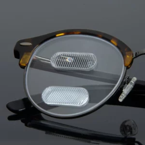 Close-up of eyeglass lenses with prism lenses attached, lying on a reflective surface.