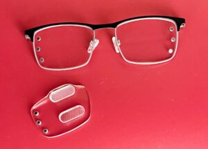 Glasses frame with magnetic prisms detached, displayed on a red background.