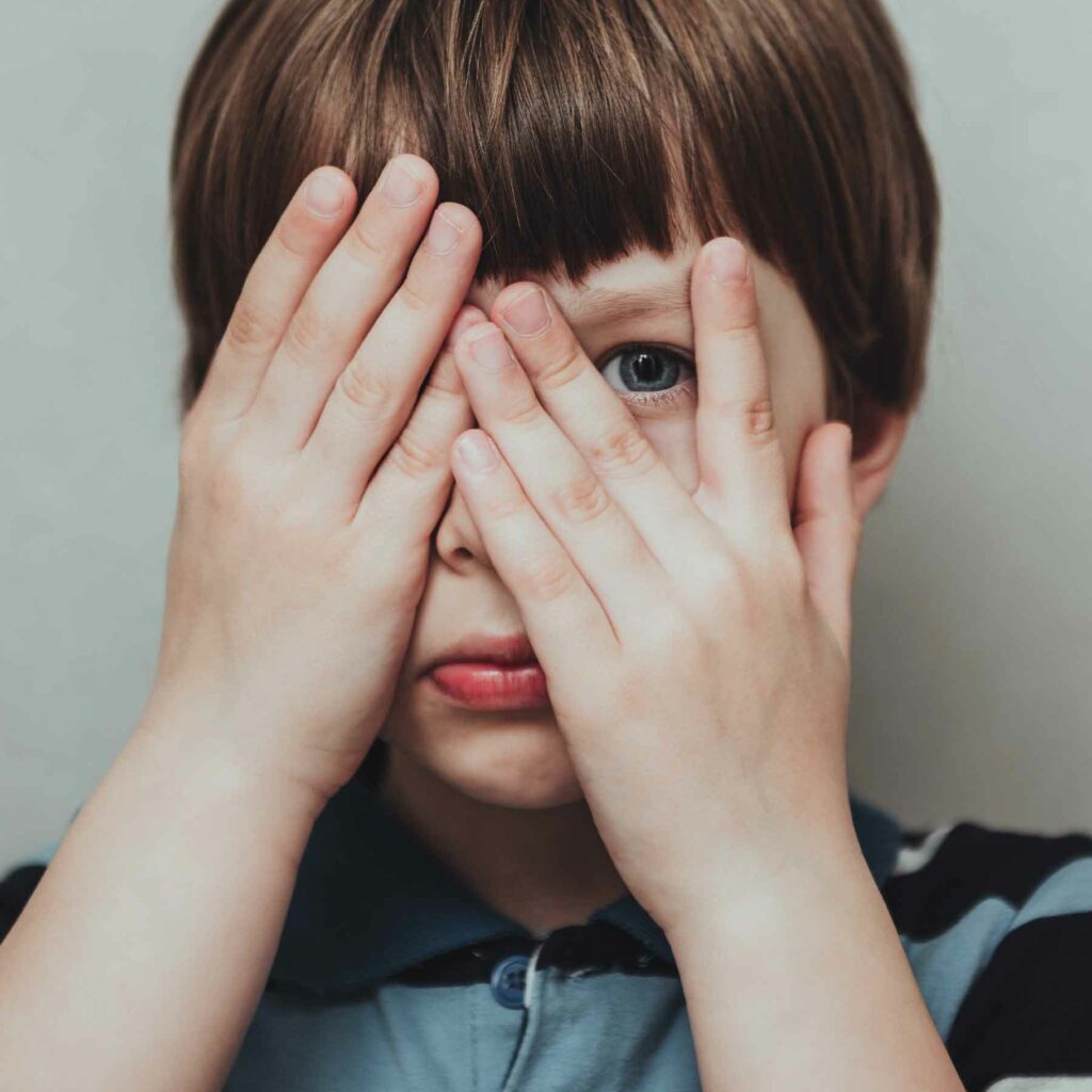 Close-up of a child peeking through fingers with a concerned expression, representing vision challenges in children.