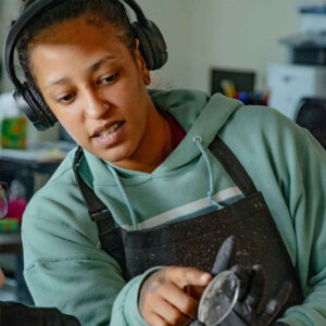 Li at Chadwick Optical, wearing headphones and a green hoodie, pointing at a lens during the AOL lens casting process.