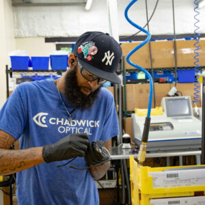 Ken at Chadwick Optical, wearing a Chadwick Optical t-shirt and gloves, working on eyeglass frames in the lab.