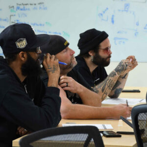 Ken, Dave, and Brian seated in a meeting at Chadwick Optical, focused on a discussion with notes in front of them.