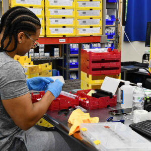 Esmerlin at Chadwick Optical organizes parts and prepares lenses at a workstation filled with yellow and red trays.