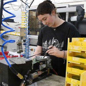 Faith assists in the lab, preparing lens blanks for processing, surrounded by equipment and storage trays.