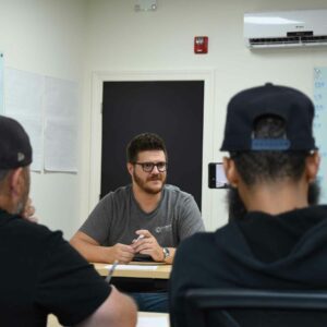 Image of Charlie at Chadwick Optical, leading a meeting, engaging with team members seated around a table in a discussion.