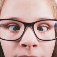 Close-up of a young girl wearing glasses with eyes misaligned, indicating a potential binocular vision issue.