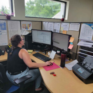 Michelle smiling while working at her computer, surrounded by office notes and decorations pinned on the cubicle walls.