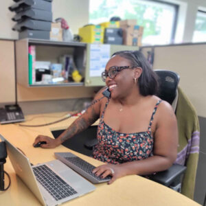 Renee at Chadwick Optical, sitting at her desk while on the phone, working on a laptop with a relaxed, friendly demeanor.