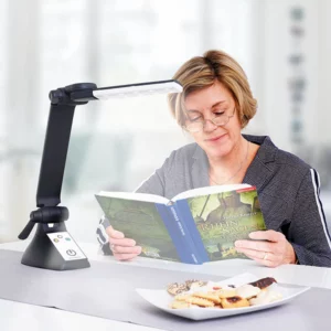 Woman reading a book under a bright LED task lamp, with cookies on a plate in the foreground.