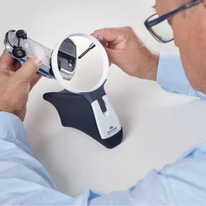 Man using a large magnifier to inspect a small toy car, highlighting a hands-free magnifying device.