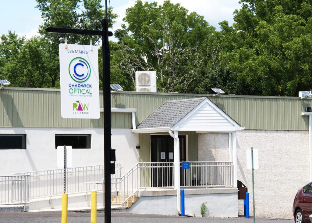 Exterior of Chadwick Optical corporate headquarters, showing a white building with green accents and a hanging sign displaying the company logo.