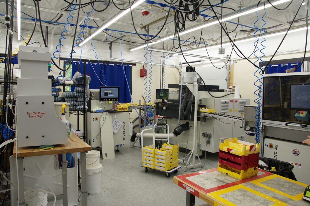 Industrial lab setup with multiple machines, hanging cables, and yellow storage bins, showcasing a manufacturing environment.