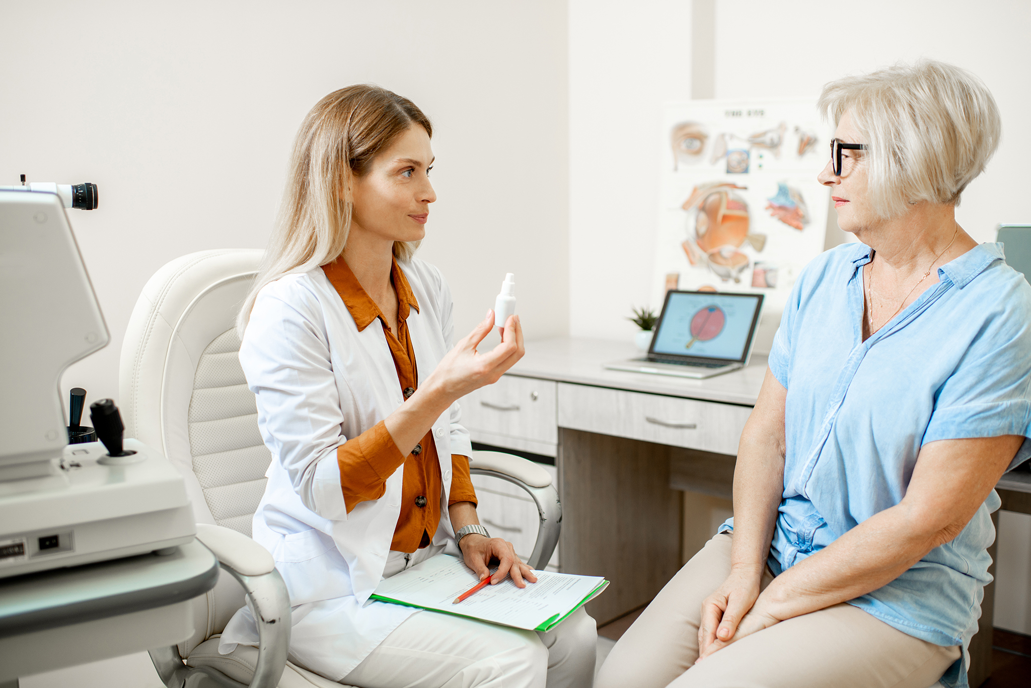 Senior woman patient talking with female ophthalmologist during Senior woman patient talking with female ophthalmologist during a medical consultation at the ophthalmologic office. Doctor offering eye medcine for a patient