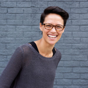 Portrait of an smiling young woman with glasses posing against gray wall