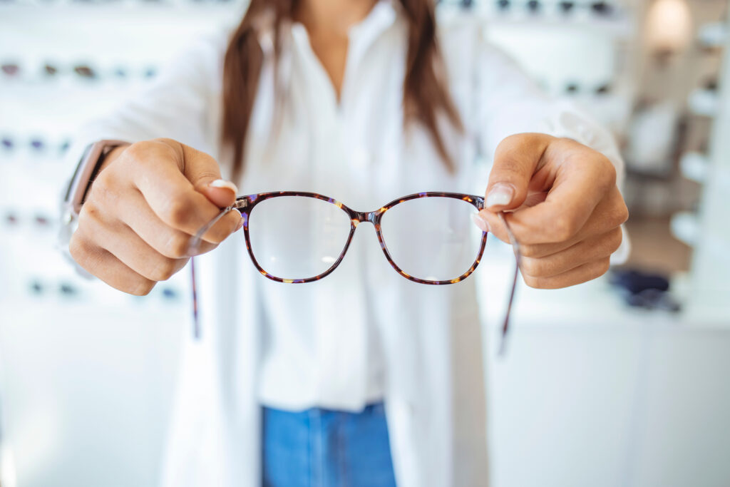 Optician,Showing,And,Suggesting,Eyeglasses,In,Optical,Shop.,Cheerful,Female Optician showing and suggesting eyeglasses in optical shop. Cheerful female ophthalmologist is working with patient. Optician giving new glasses to customer for testing and trying.