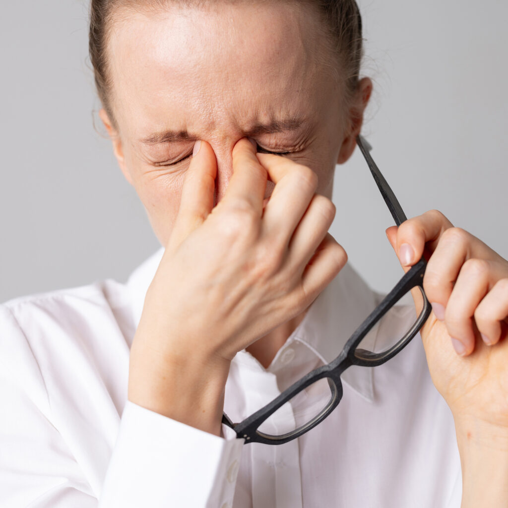 Woman takes off her glasses and holds her eyes in pain, concept of optics, glasses selection and vision problems