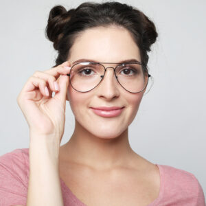 Closeup of attractive young woman isolated on gray background, wearing big spectacles with thin black frame, touching temples with fingers, smiling with expression of satisfaction and interest.