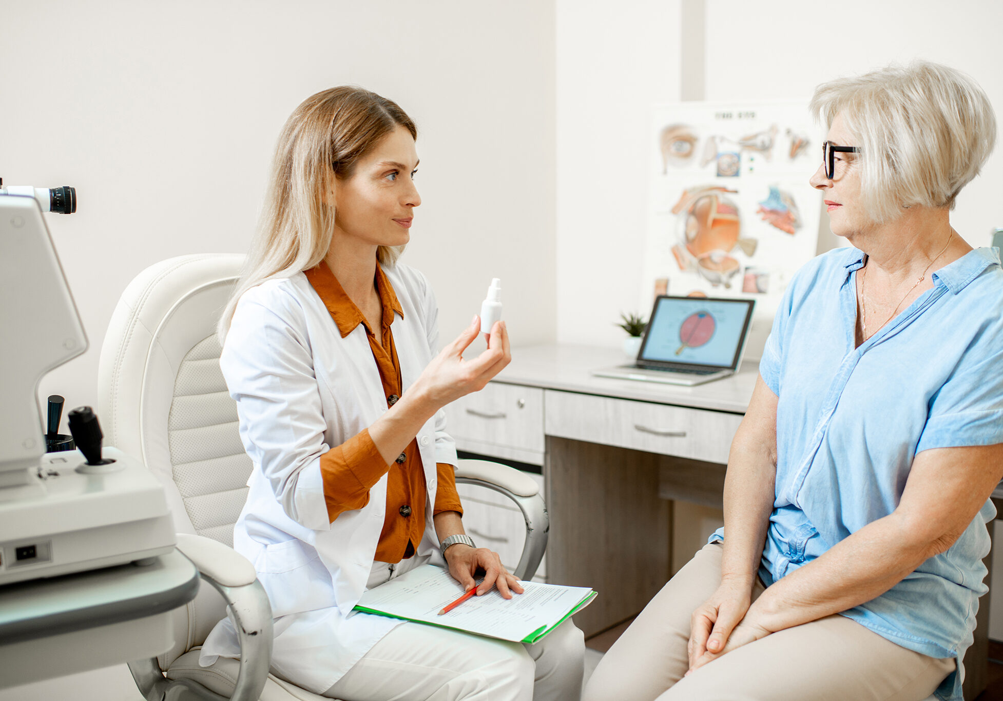 Senior woman patient talking with female ophthalmologist during a medical consultation at the ophthalmologic office. Doctor offering eye medcine for a patient