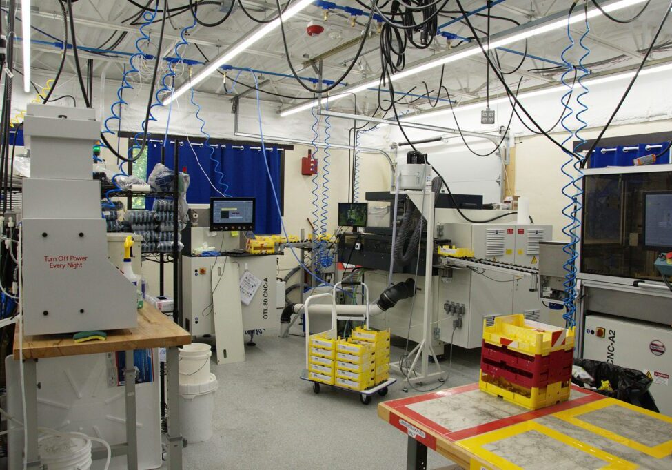 Industrial lab setup with multiple machines, hanging cables, and yellow storage bins, showcasing a manufacturing environment.
