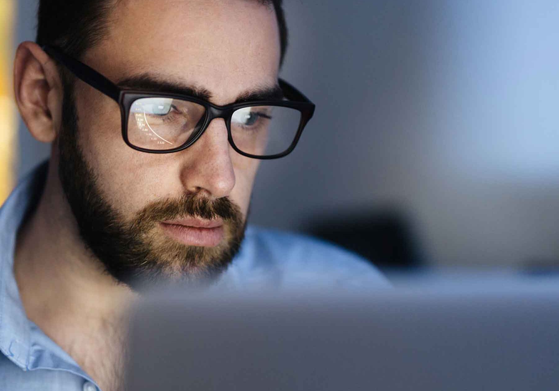 Man wearing glasses working at a computer, focusing intently, illustrating the strain related to convergence issues while using digital screens.